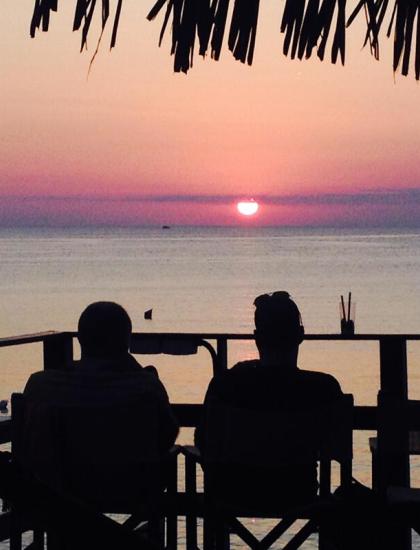 Sonnenuntergang über dem Meer mit zwei silhouettierten Personen.