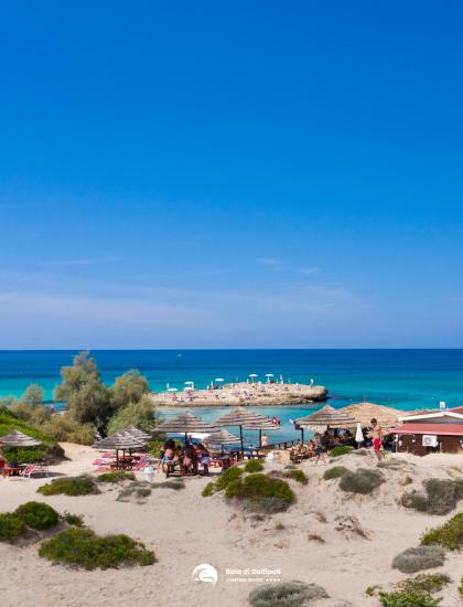 Beach with white sand, blue sea, and kiosks.