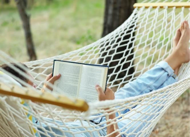 Persona su un'amaca legge un libro all'aperto.