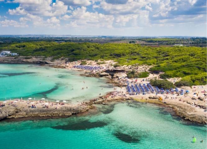 Beach with blue umbrellas and turquoise sea, surrounded by greenery.